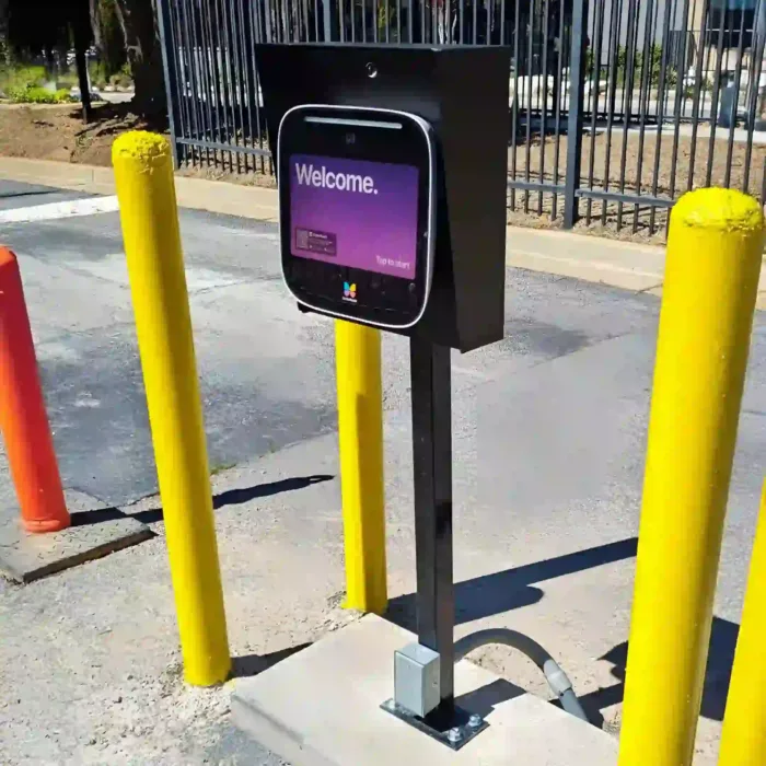 Video intercom mounted on a pedestal between yellow bollards at a vehicle gate