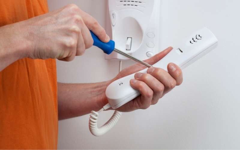 Maintenance worker repairs a broken in-unit door phone intercom.