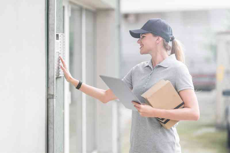 Delivery courier using an intercom at a delivery door.