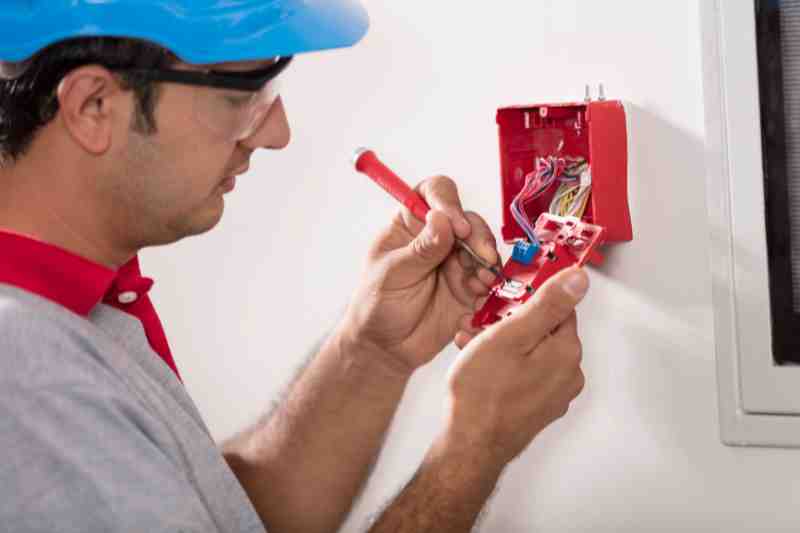 Installer fixing and troubleshooting a fire alarm system.