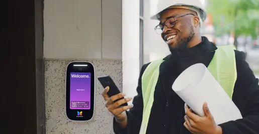 Developer wearing reflective vest and hard hat while holding blueprint and smiling at phone in front of building