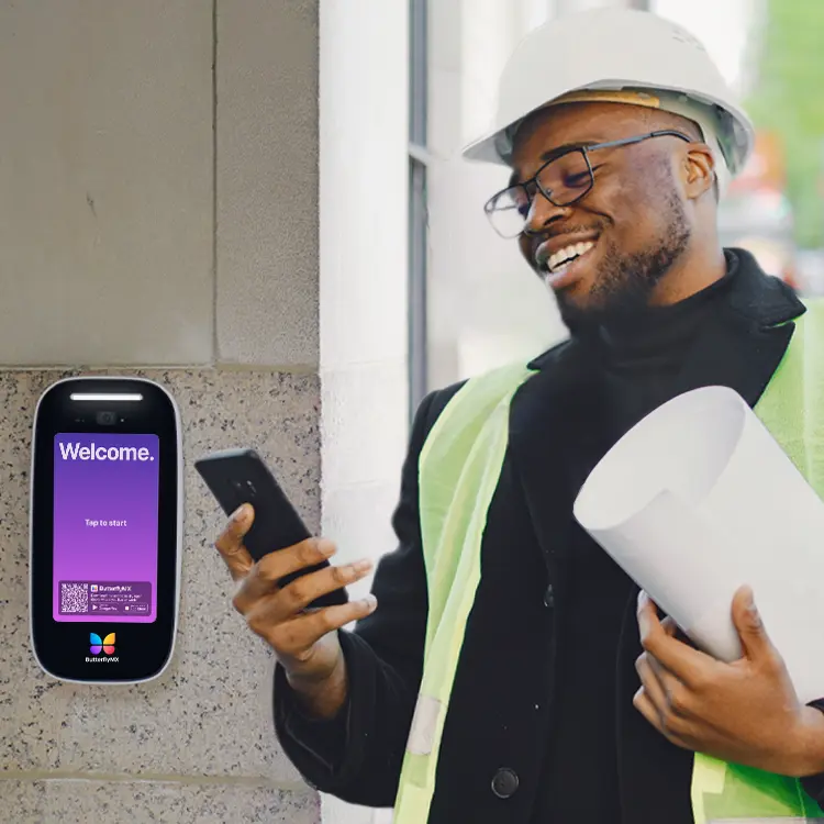 male developer standing in front of butterflymx intercom outside building entrance and smiling at his phone while wearing high visibility vest and hard hat