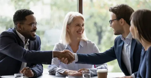 group of people smiling and shaking hands while sitting at an office meeting table