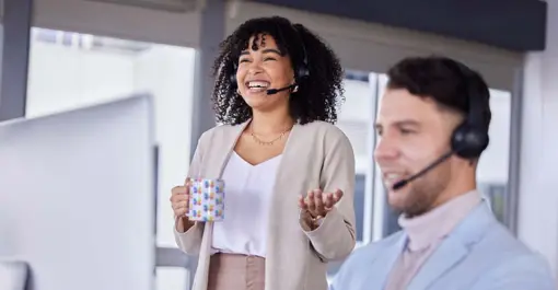 woman wearing headset smiling in conversation in front of desktop computer while holding butterflymx coffee mug