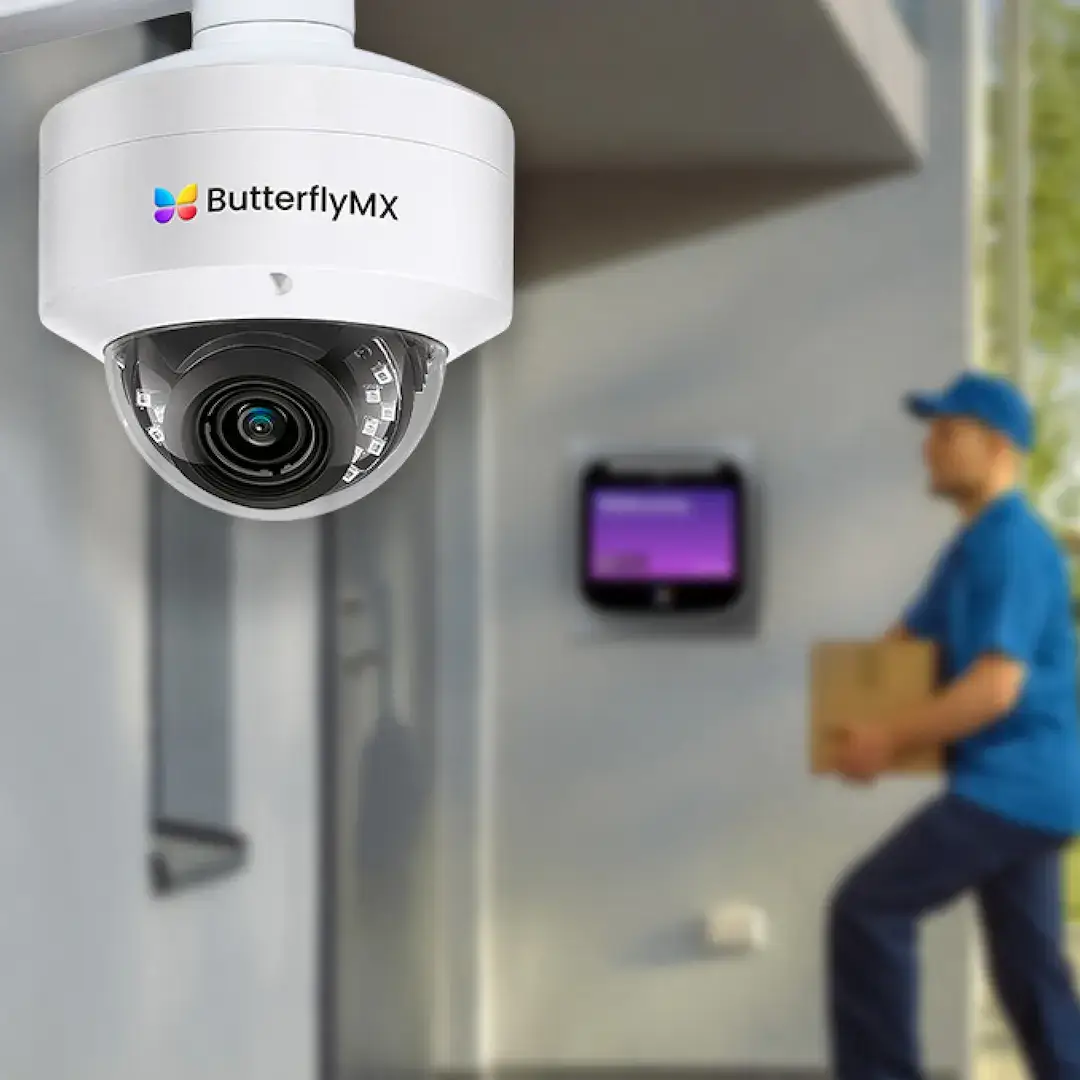 delivery person brings package to building entrance in front of ButterflyMX video intercom, with ButterflyMX dome security camera above