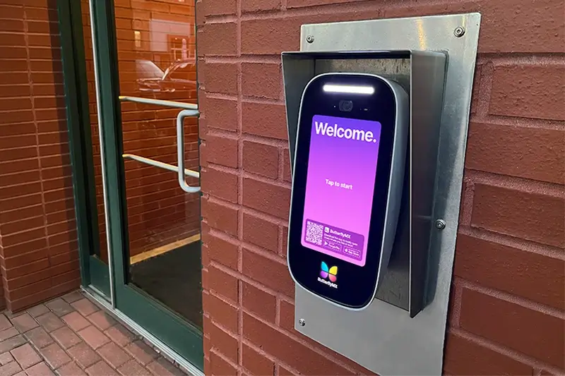 ButterflyMX Video Intercom installed on a brick wall near a multifamily property front door.